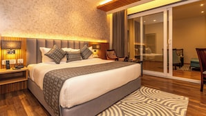 A modern bedroom with a large bed, wooden headboard, bedside tables with lamps, a patterned rug, and a sliding glass door leading to a balcony.