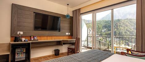 Une chambre d’hôtel dotée d’un grand lit, d’un téléviseur à écran plat fixé au mur, d’un mini-réfrigérateur, d’une petite table avec une chaise et d’un balcon offrant une vue sur la montagne.