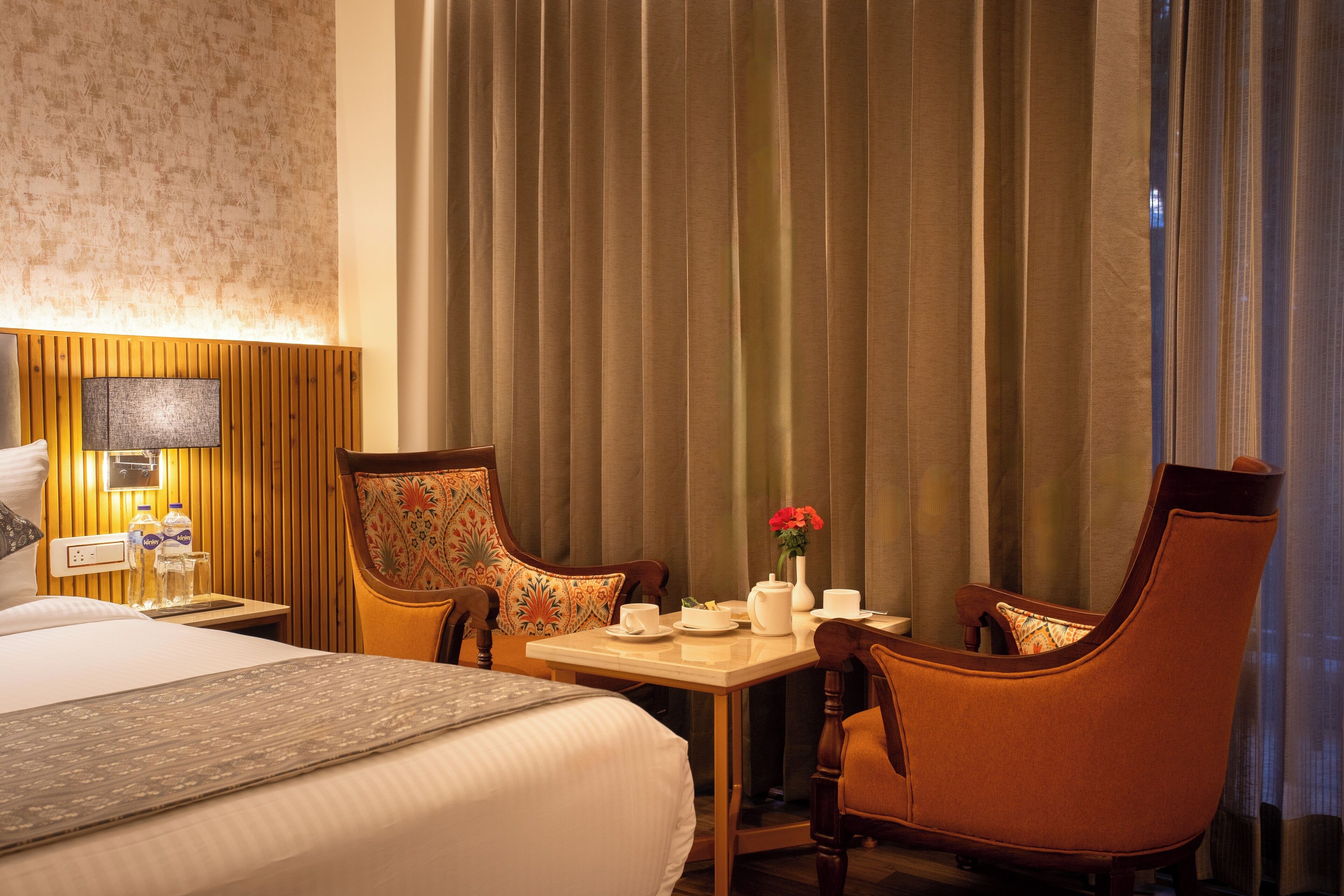 Ein Hotelzimmer mit einem Bett, einem Nachttisch mit Lampe, einem Tisch mit Blumenvase und zwei Stühlen.