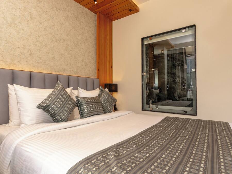 A bedroom with a large bed, a wooden headboard, a mirror, and a nightstand with a lamp and a bottle.