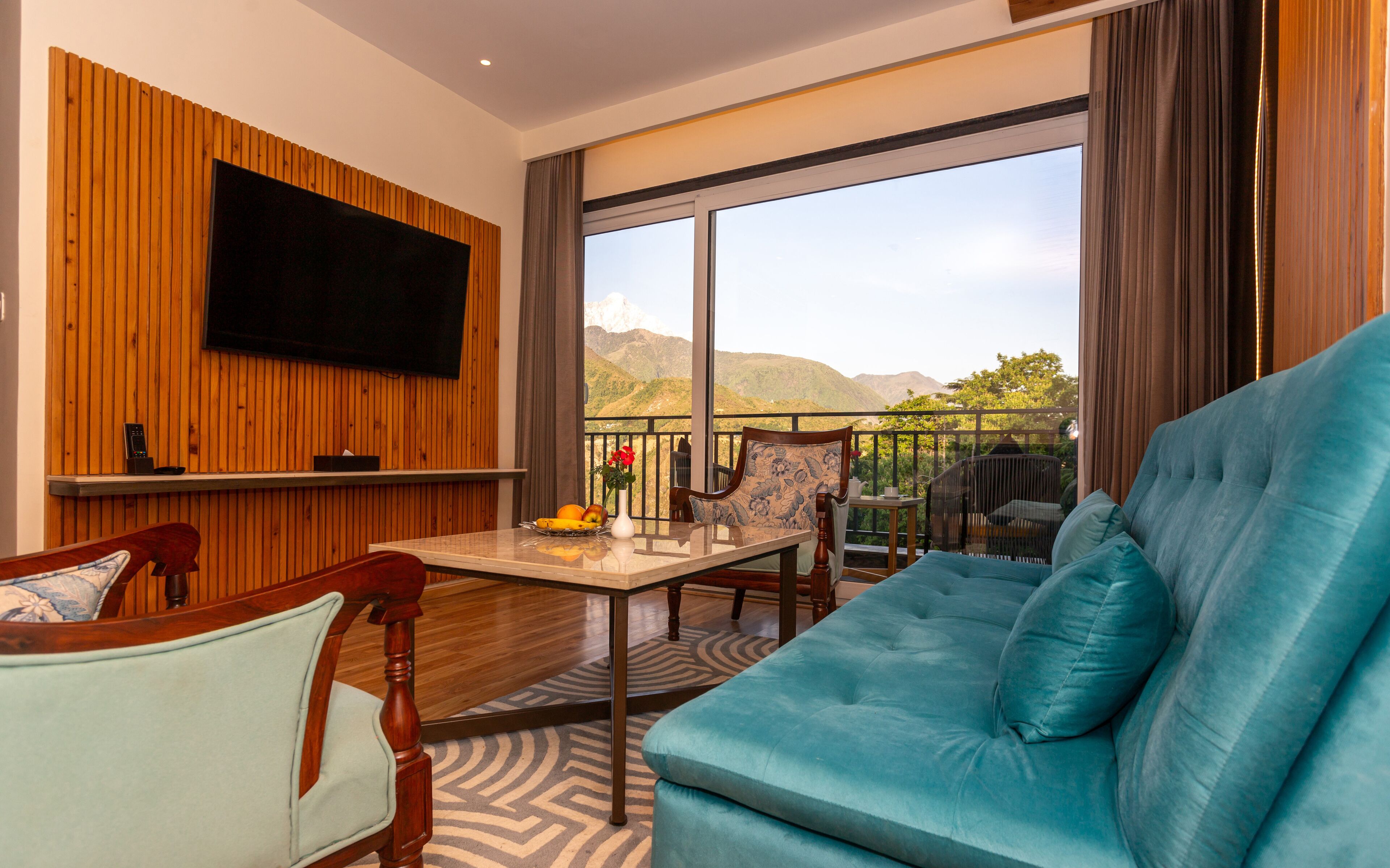 A modern living room with a large sofa, a dining table, and a TV mounted on a wooden wall.
