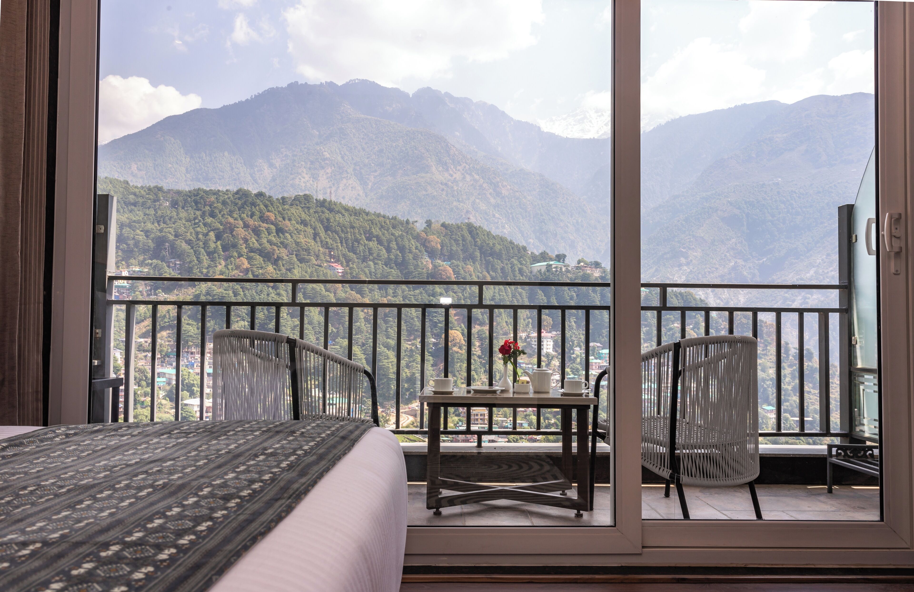A balcony with a bed, a table with a vase of flowers, and chairs.