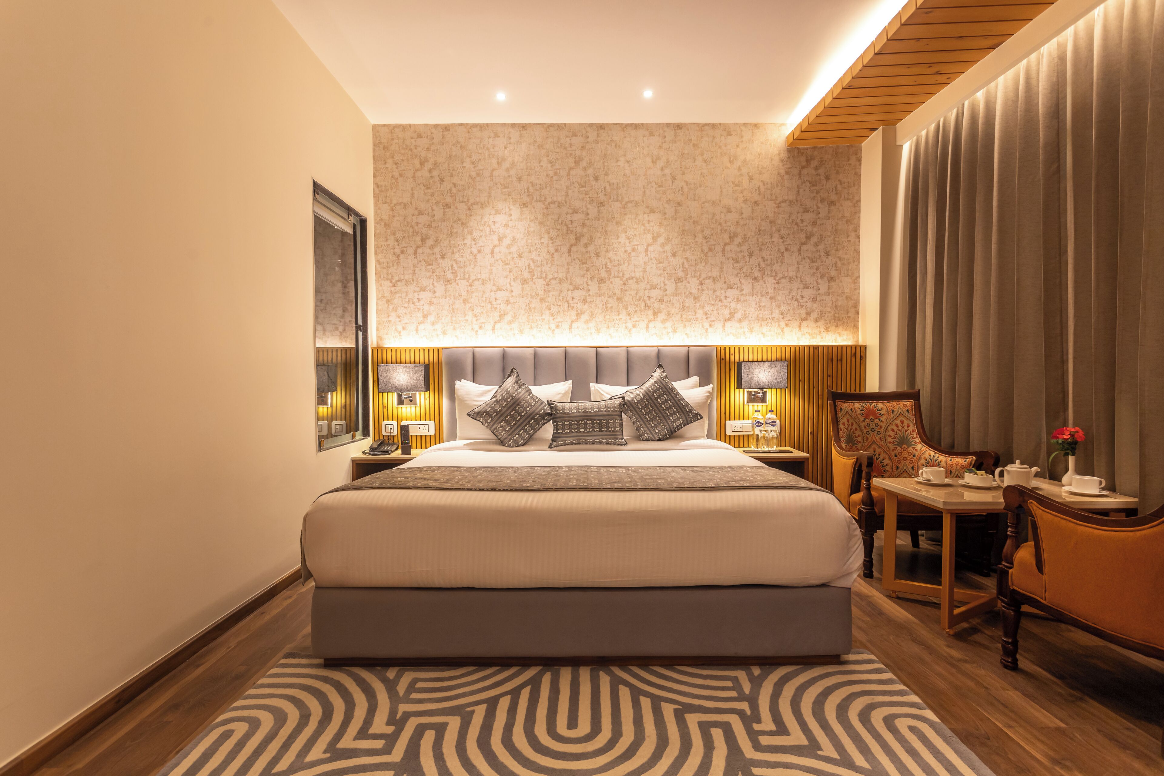 Une chambre d’hôtel moderne avec un grand lit, une petite table avec une chaise et une grande fenêtre avec des rideaux.