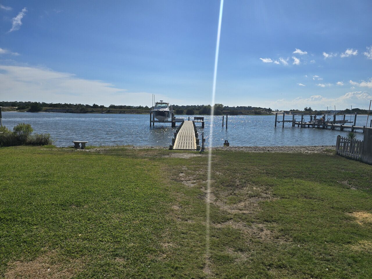 A grassy area with a dock extending into a body of water, a bench, and a small structure on the dock.