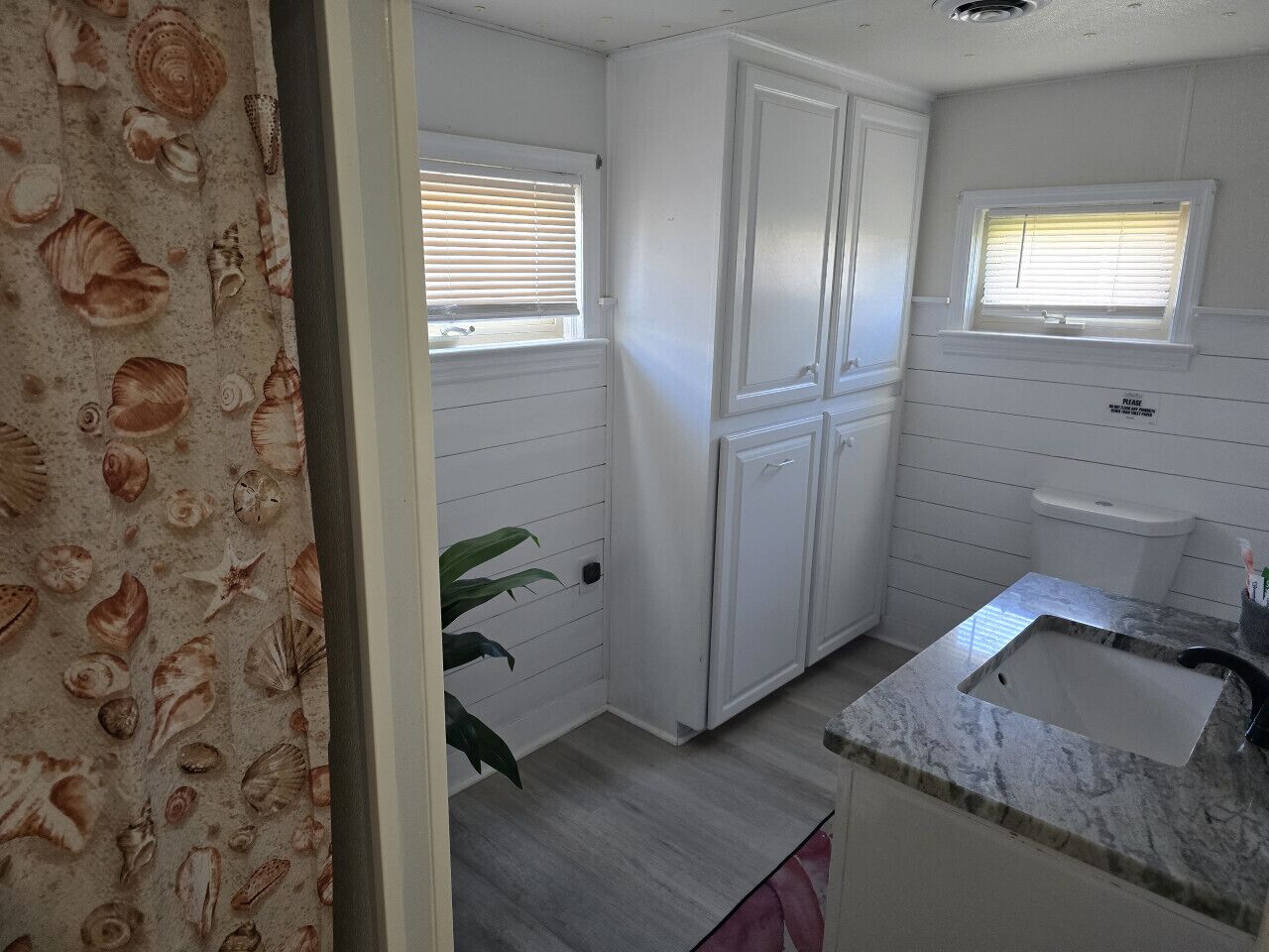 A small kitchen with white cabinets, a sink, and two windows with blinds.