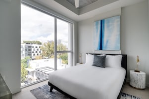 Un dormitorio moderno con una cama grande, vistas a la ciudad y un cuadro abstracto azul.