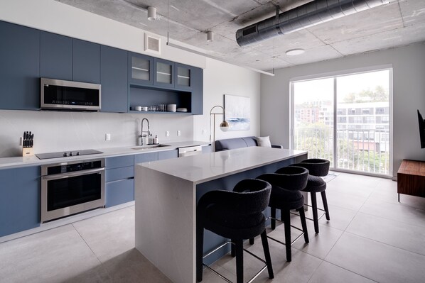 A modern kitchen with a central island, bar stools, and a large window with a city view. - Kasa Wynwood Miami (Miami)