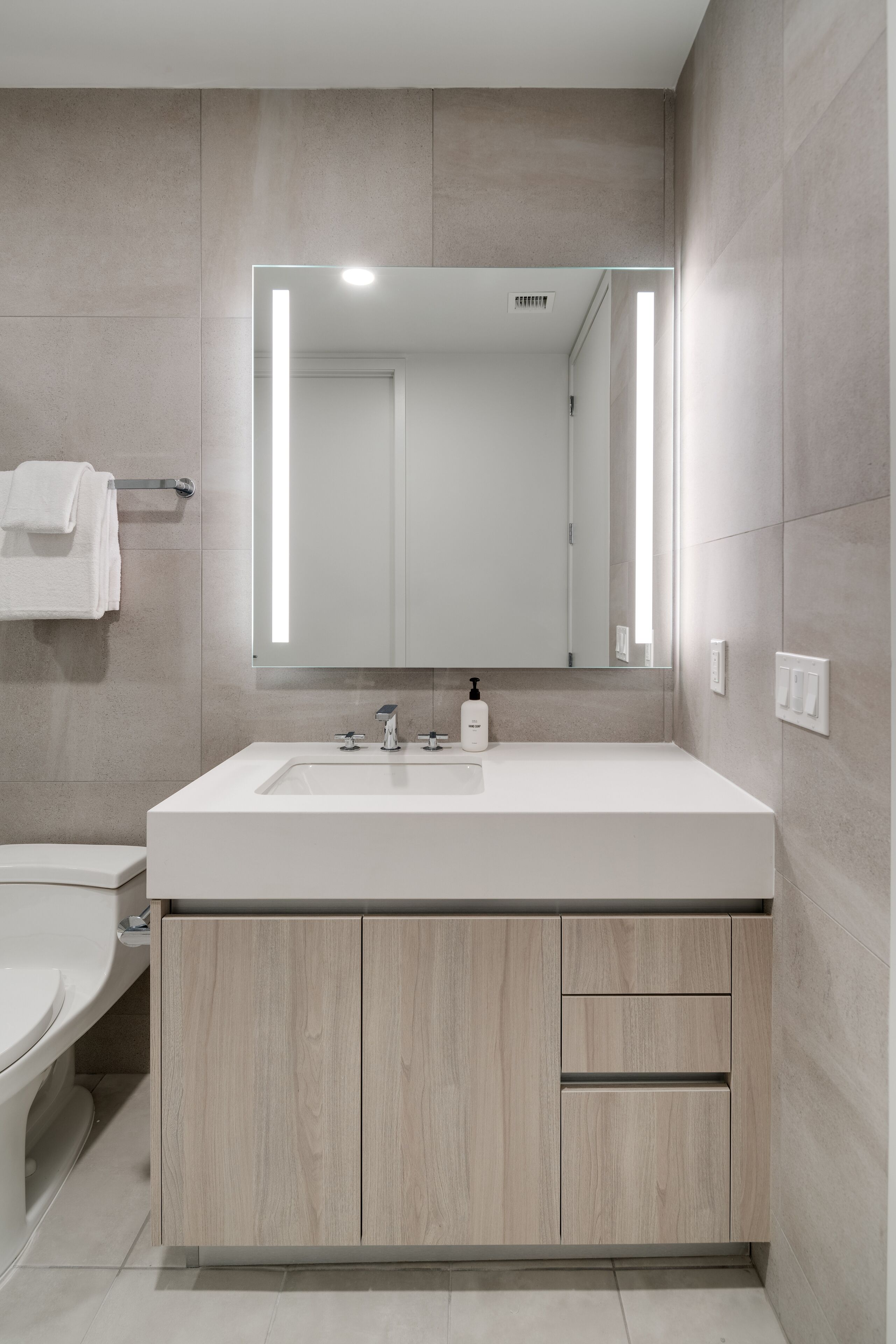 Un baño moderno con un lavabo blanco, armarios de madera y un espejo grande.