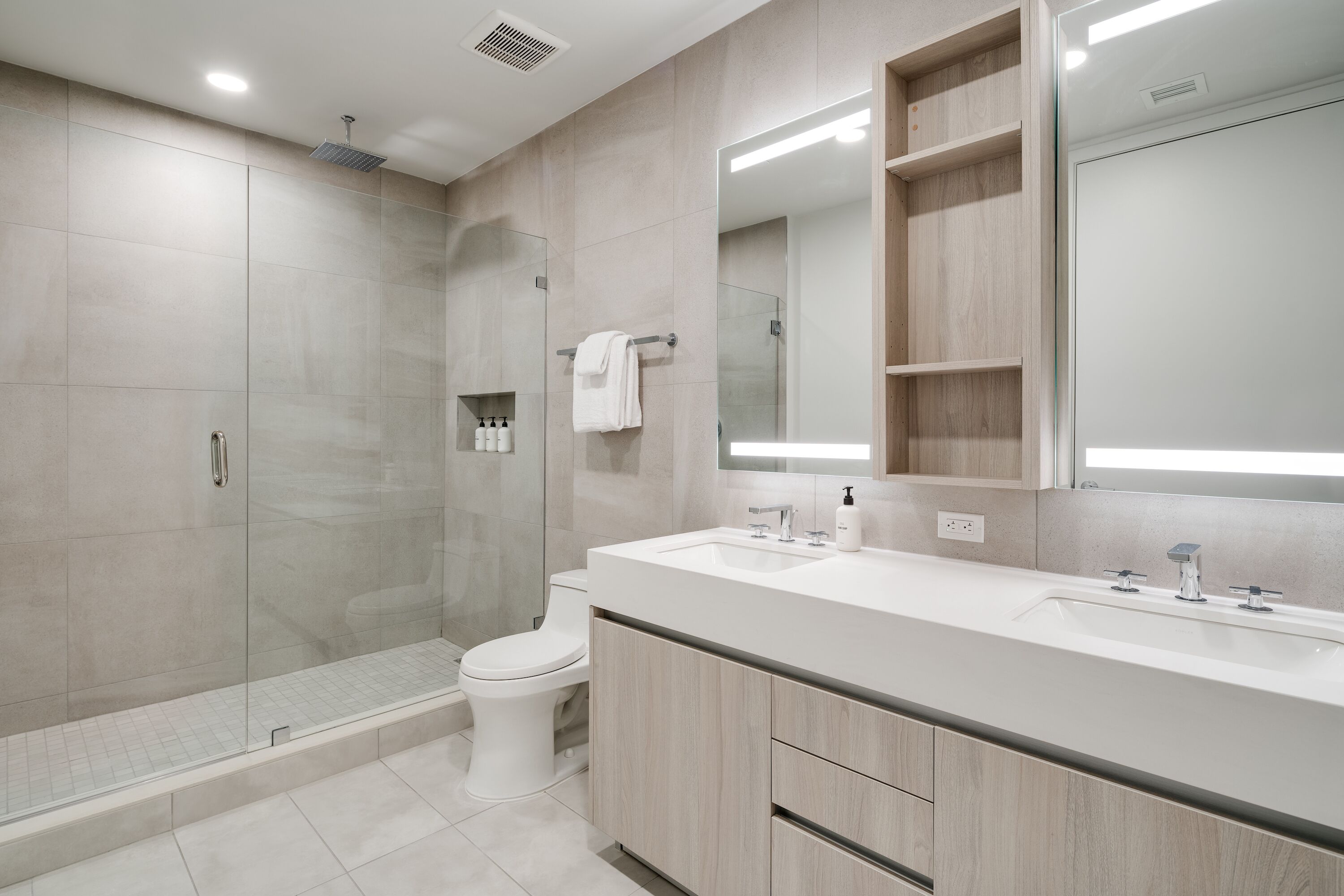 A modern bathroom with a glass shower enclosure, a toilet, a sink with a mirror, and wooden cabinets.