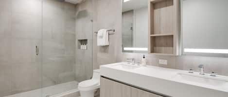 A modern bathroom with a glass shower enclosure, a toilet, a sink with a mirror, and wooden cabinets.