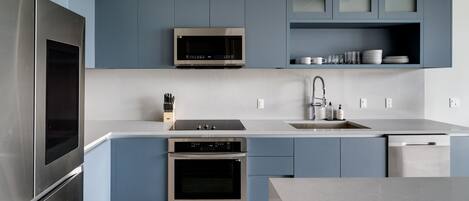 A modern kitchen with stainless steel appliances, blue cabinetry, and a white countertop.