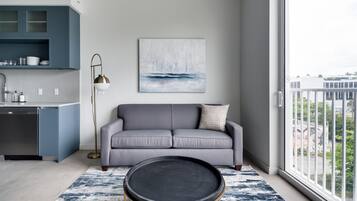A modern living room with a grey sofa, a round black coffee table, and a painting of a sailboat on the wall.
