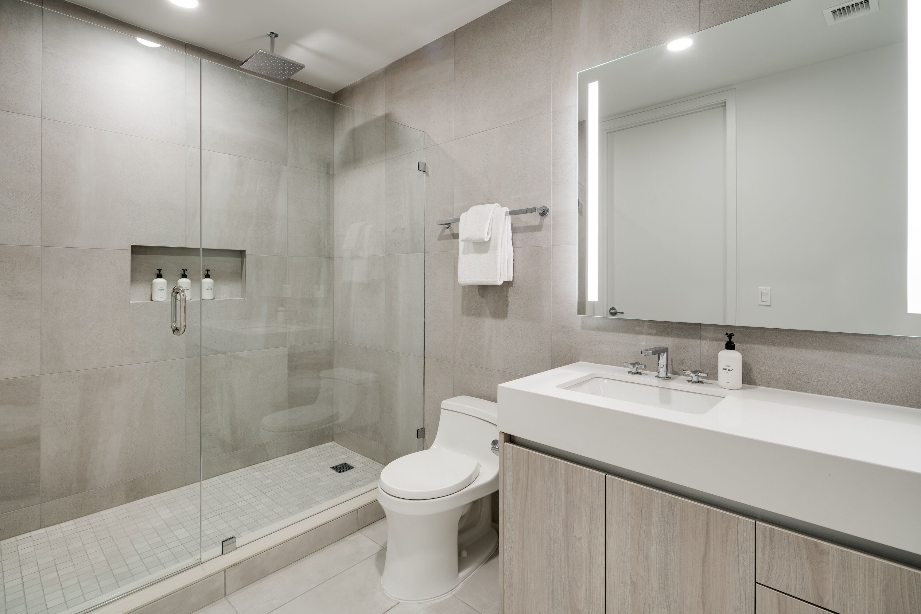 A modern bathroom with a glass-enclosed shower, a toilet, and a vanity with a mirror.