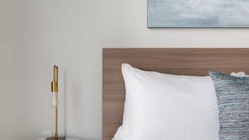 A modern hotel room with a wooden headboard, a white bed with a blue and white patterned pillow, and a marble side table with a gold lamp.