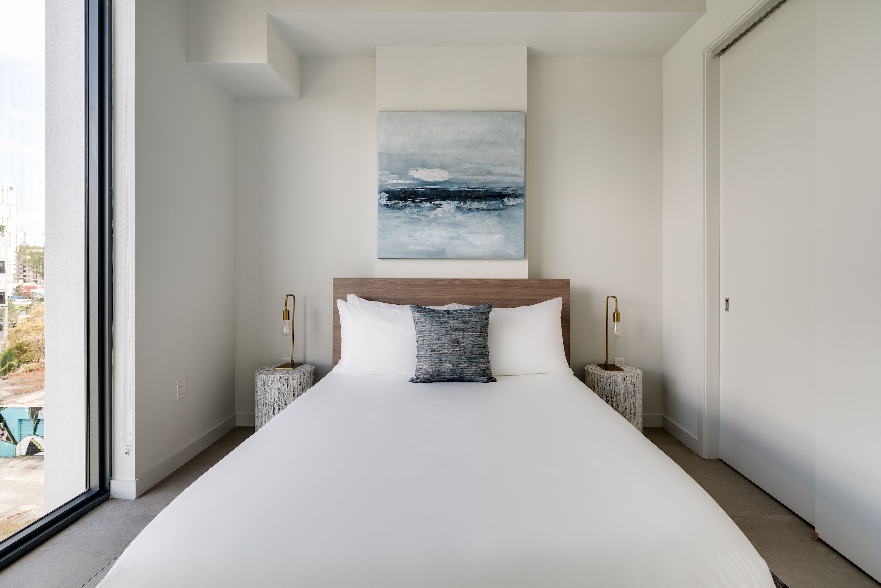 A modern bedroom with a large bed, a view of the sea through the window, and a minimalist design.