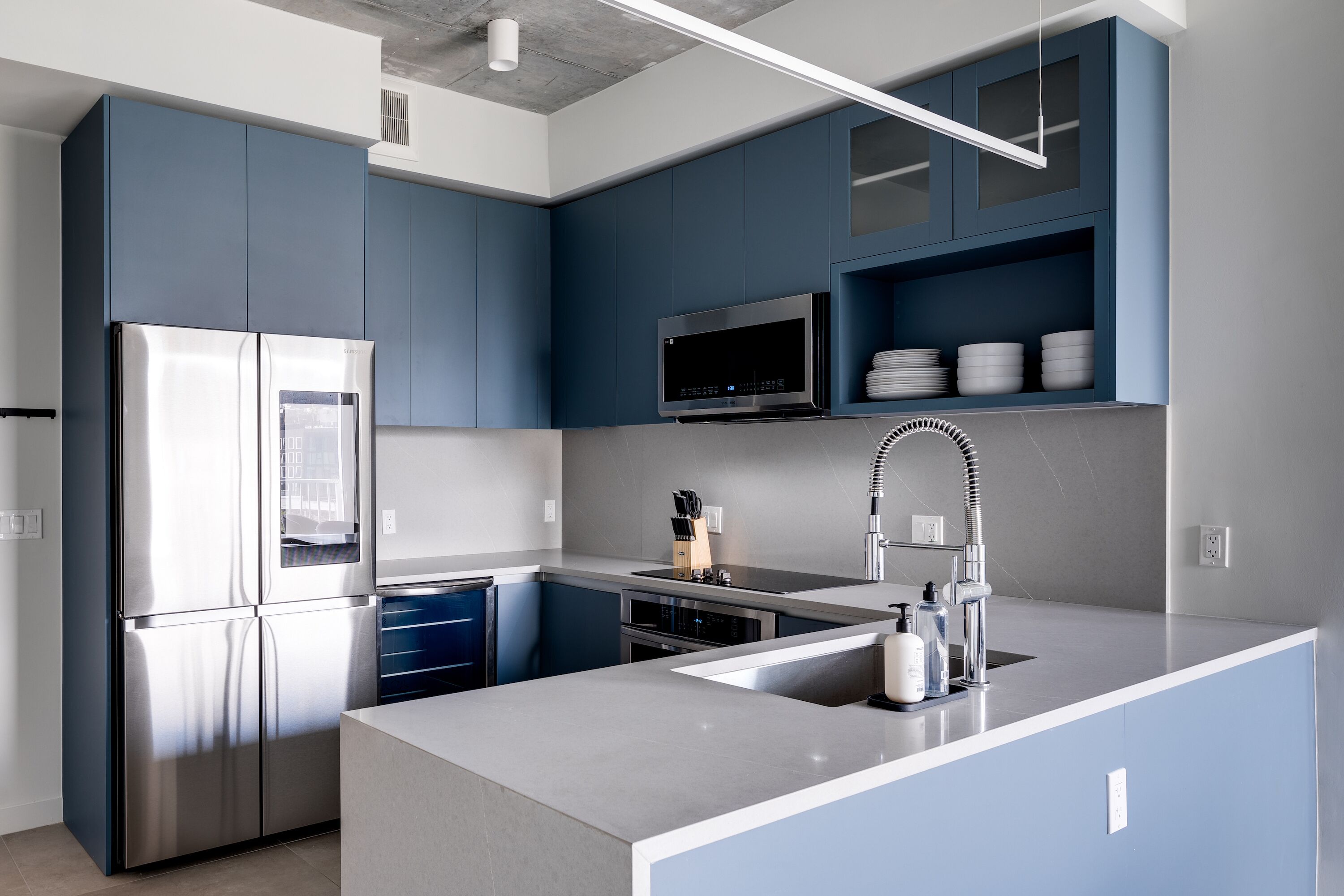 A modern kitchen with blue cabinets, stainless steel appliances, and a central island with a sink.