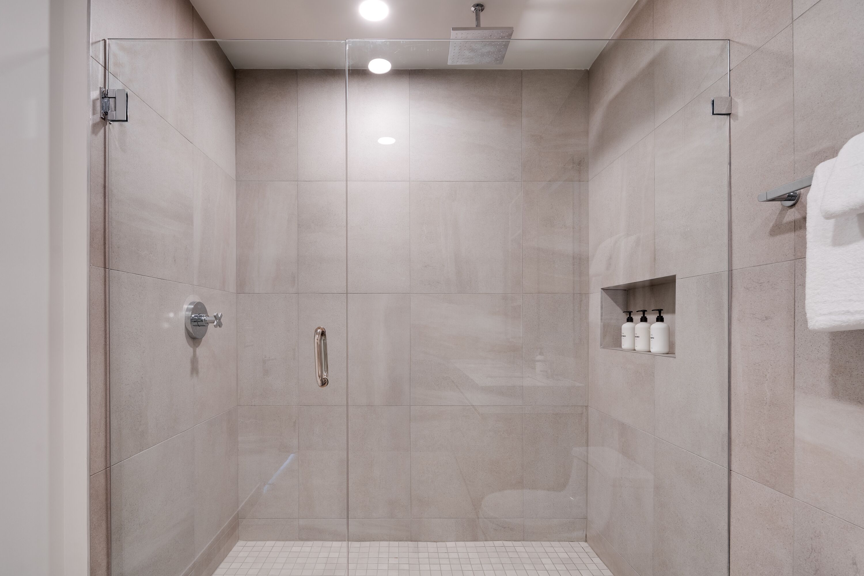 A modern shower area with a glass door, a hand dryer, and a shelf with toiletries.