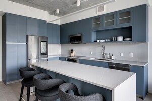 Una cocina moderna con una isla grande, taburetes de bar, electrodomésticos de acero inoxidable y armarios azules.