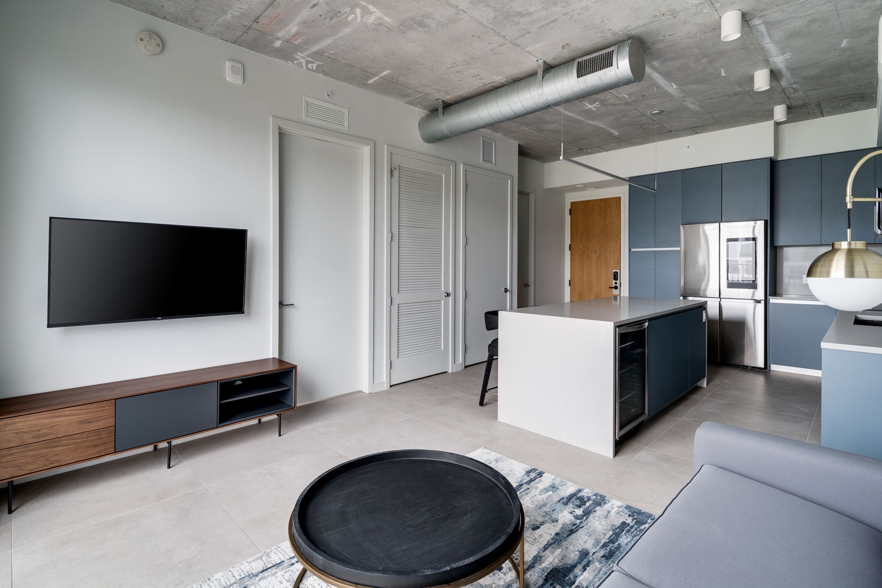 A modern living space with a flat-screen TV, a dining area, and a kitchen with stainless steel appliances.