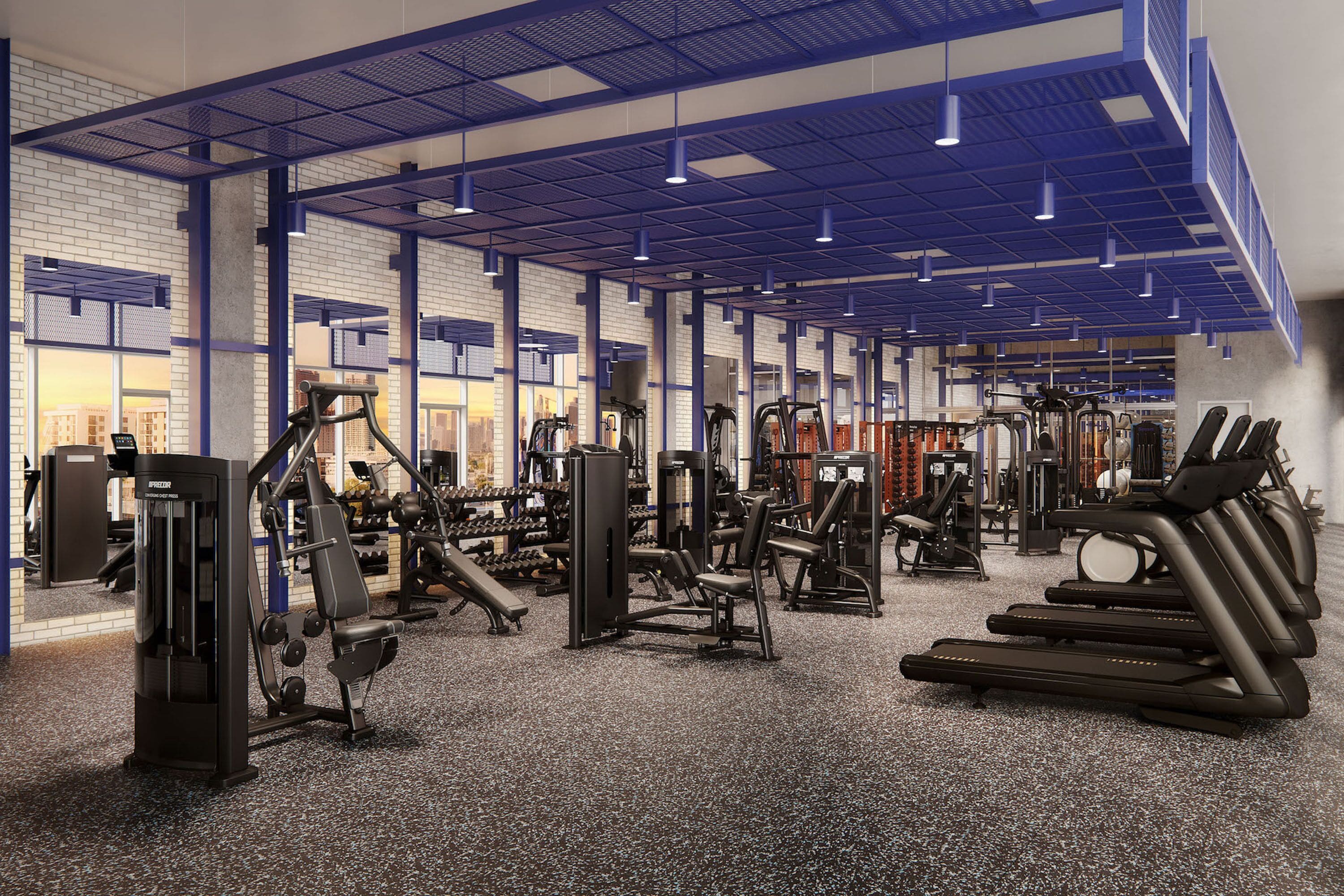 A gym with various exercise equipment, including treadmills and weight machines, and a high ceiling with blue structural beams.