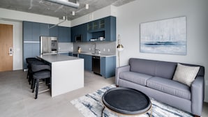 A modern kitchen with blue cabinets, a central island, and a grey sofa in a living area. - Kasa Wynwood Miami (Miami)