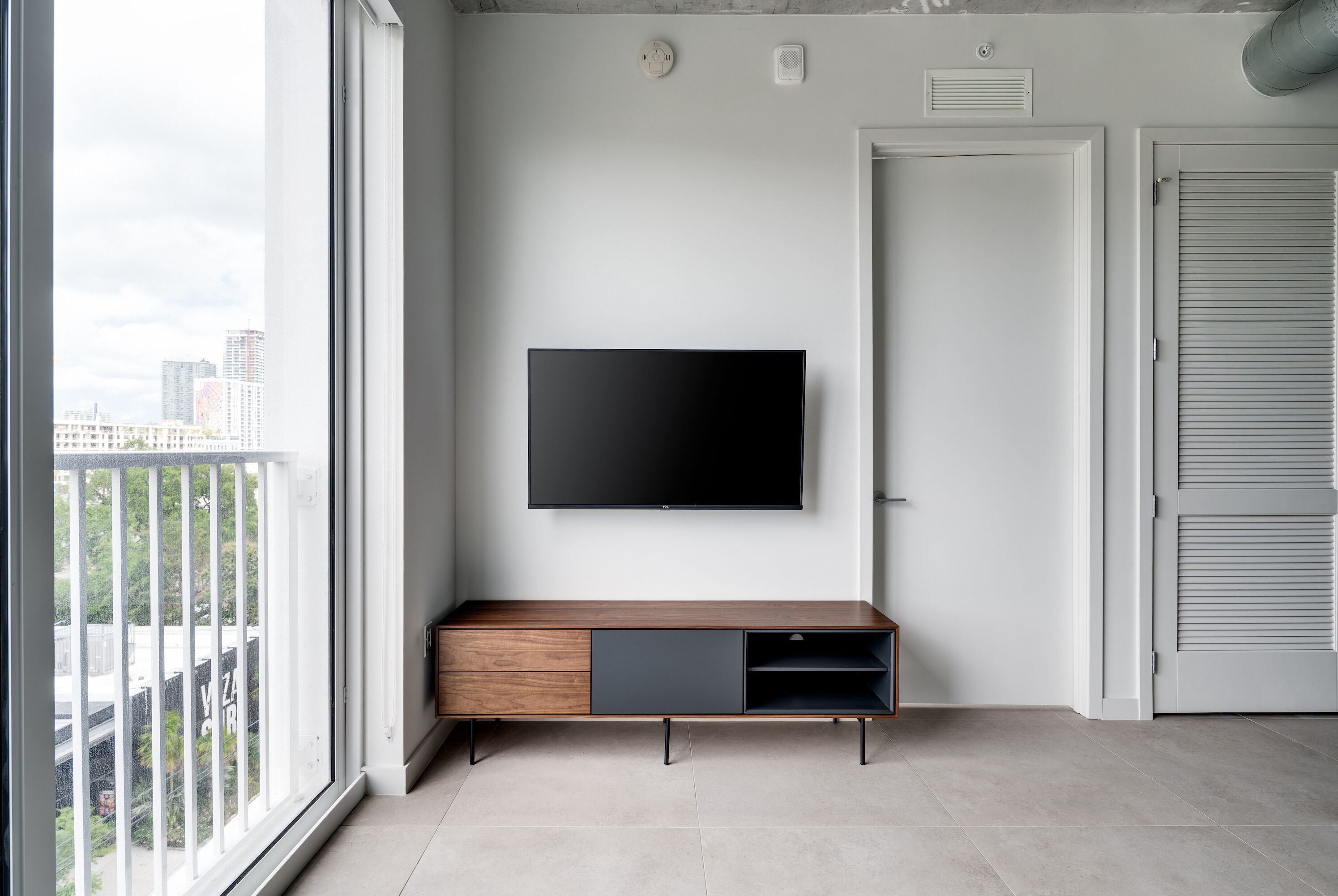 A modern living room with a large TV mounted on the wall, a wooden cabinet with a black drawer, and a sliding door.