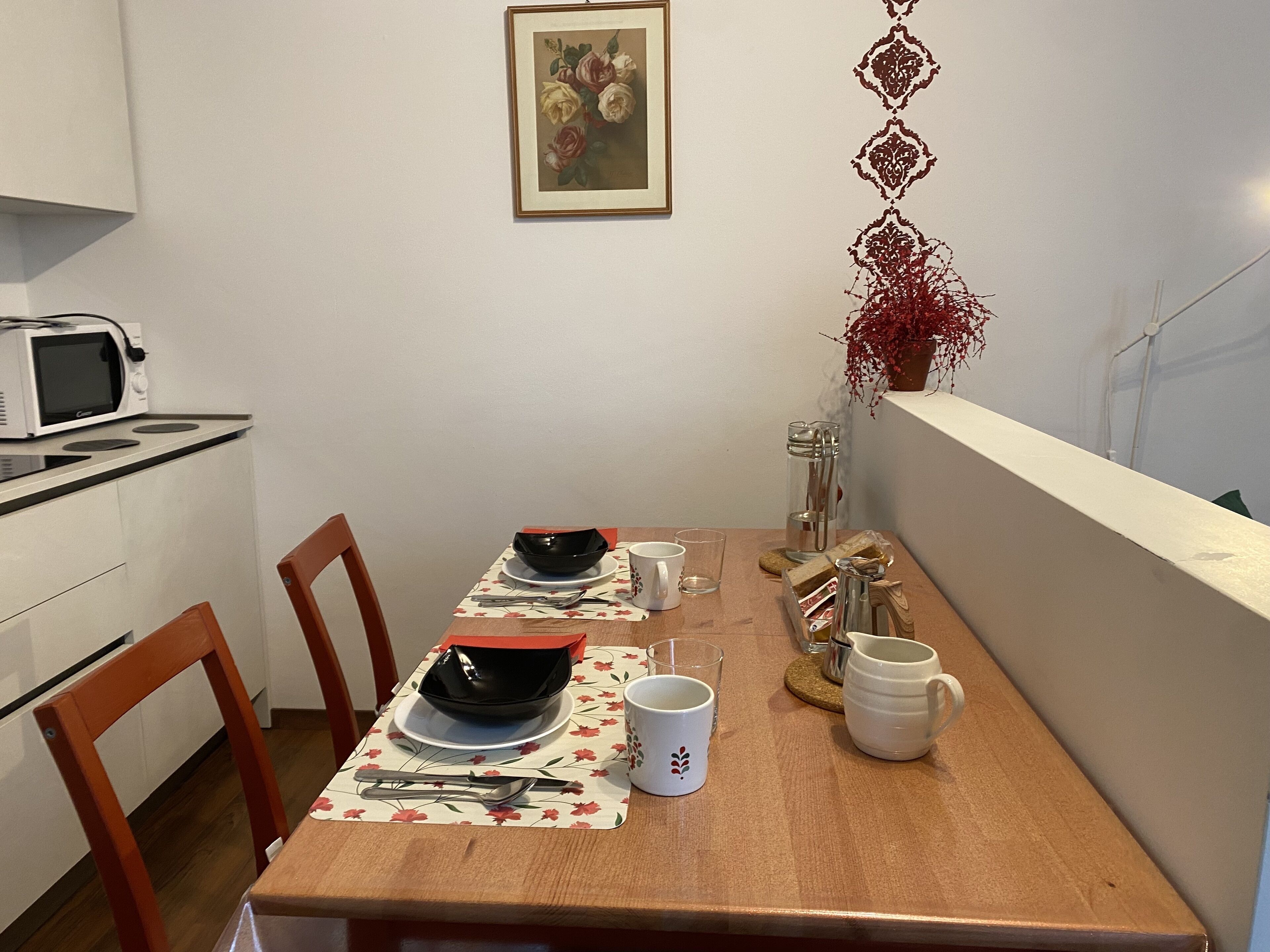 Un comedor con una mesa de madera dispuesta para dos personas, un microondas y una planta en maceta.
