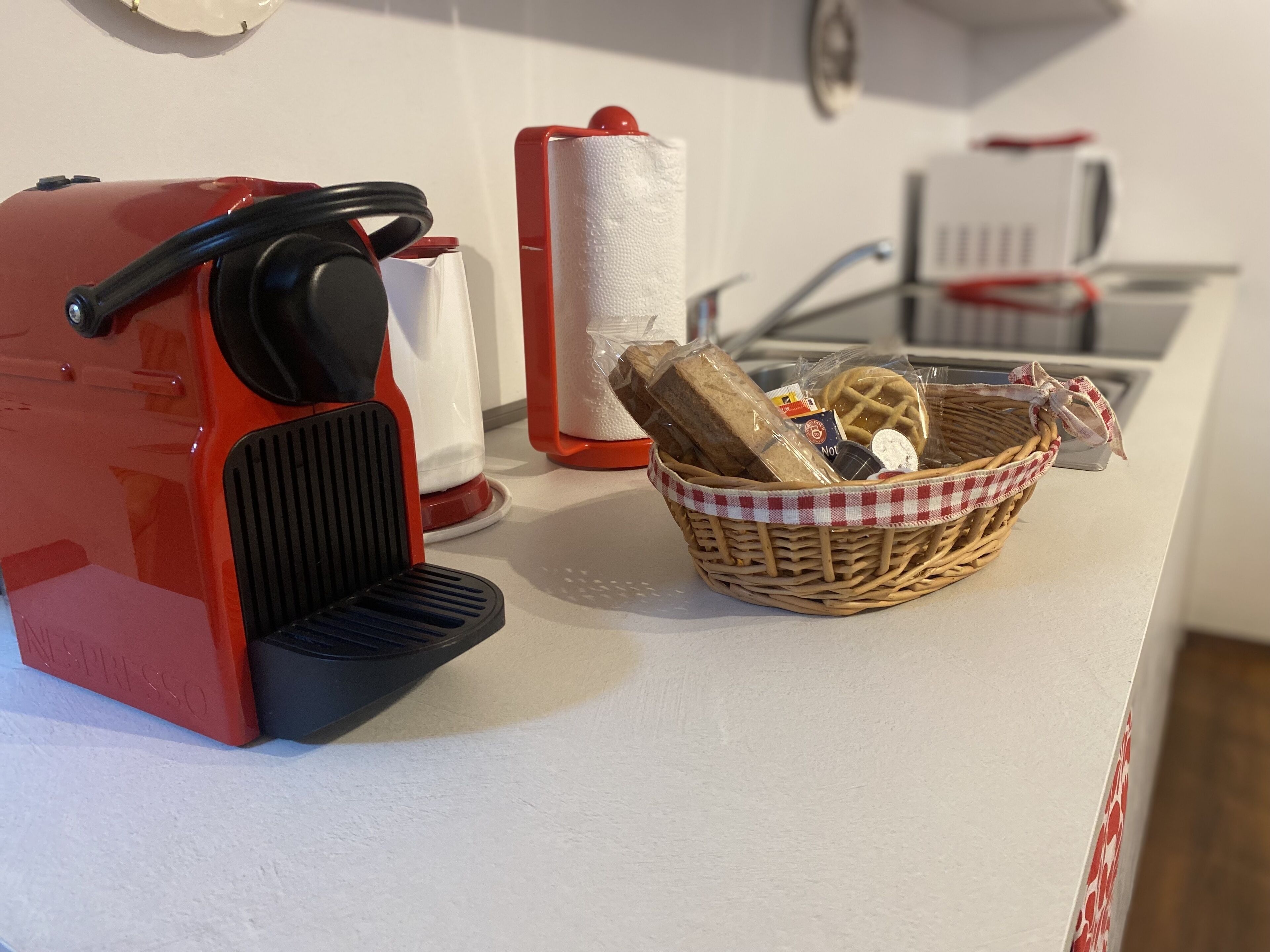 A kitchen counter with a red espresso machine, a basket of bread, and a white cloth.