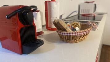 A kitchen counter with a red espresso machine, a basket of bread, and a white cloth.