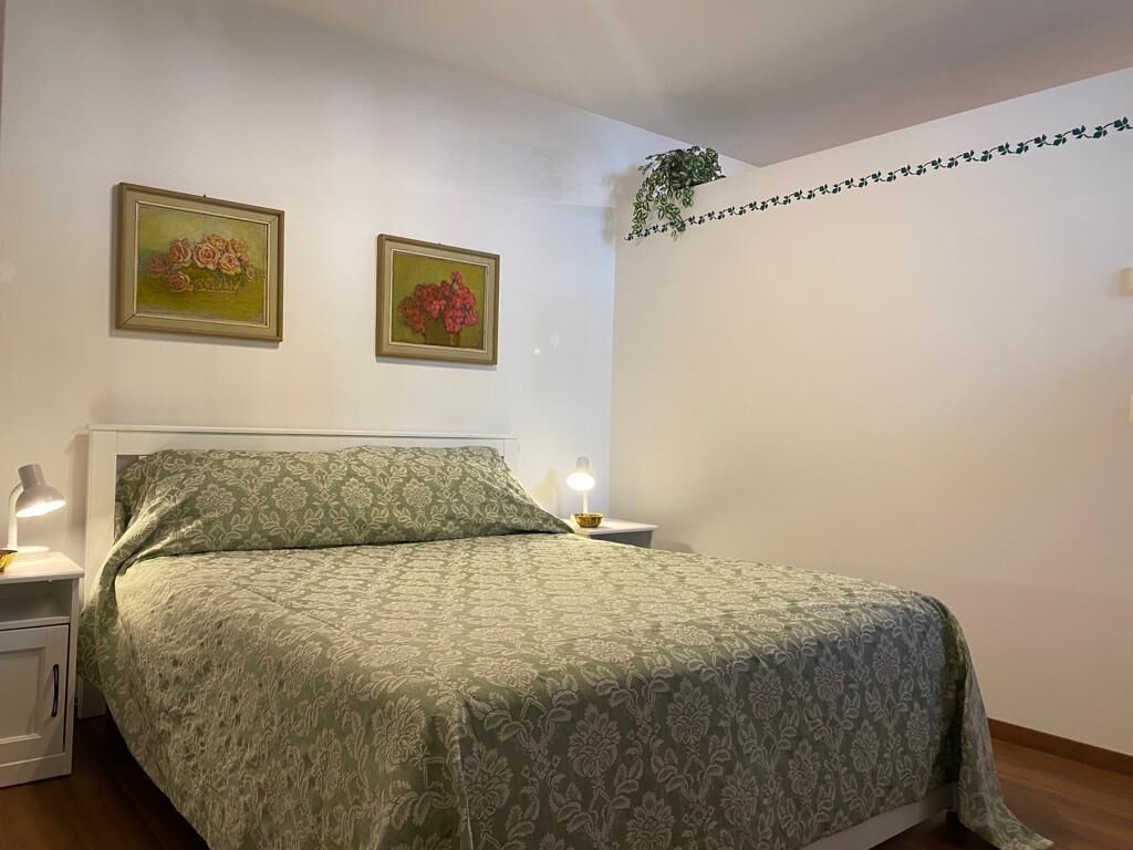 Quarto com cama, duas luminárias de parede e duas pinturas florais emolduradas.