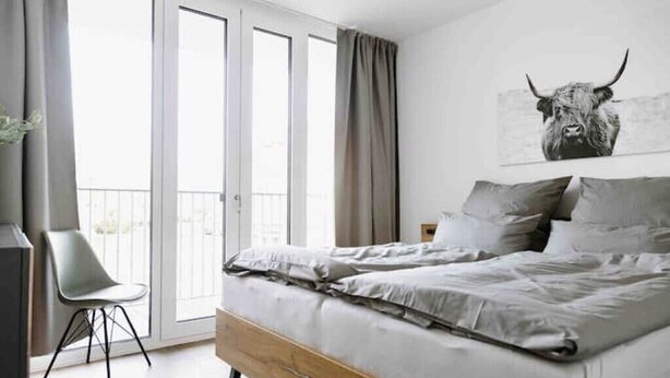 Une chambre à coucher avec un lit, une chaise et une grande fenêtre avec des rideaux.