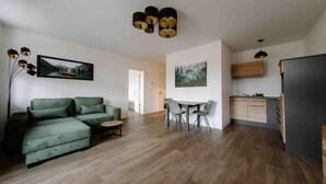Un salon moderne avec un canapé vert, une table à manger avec des chaises et un coin cuisine doté de meubles en bois.