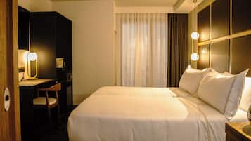 Una habitación de hotel con una cama grande, un escritorio con una silla, un espejo y una ventana con cortinas.