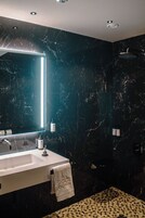 Un bagno moderno con una parete in marmo, uno specchio grande, un lavandino e una doccia.