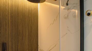 A modern shower with a wooden panel wall, a glass door, and marble-like wall tiles.