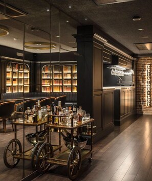 A library with bookshelves, a bar cart with bottles, and a brick wall.