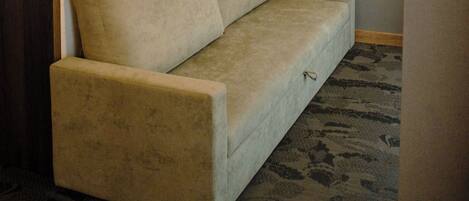 Un sofá de tonos neutros con cabecera de madera en una habitación con alfombra estampada y una lámpara fijada a la pared.