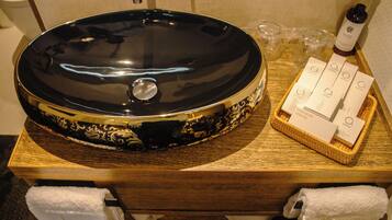 A black and gold oval-shaped sink with a lid, a wooden tray with toiletries, and a white towel on a wooden surface.