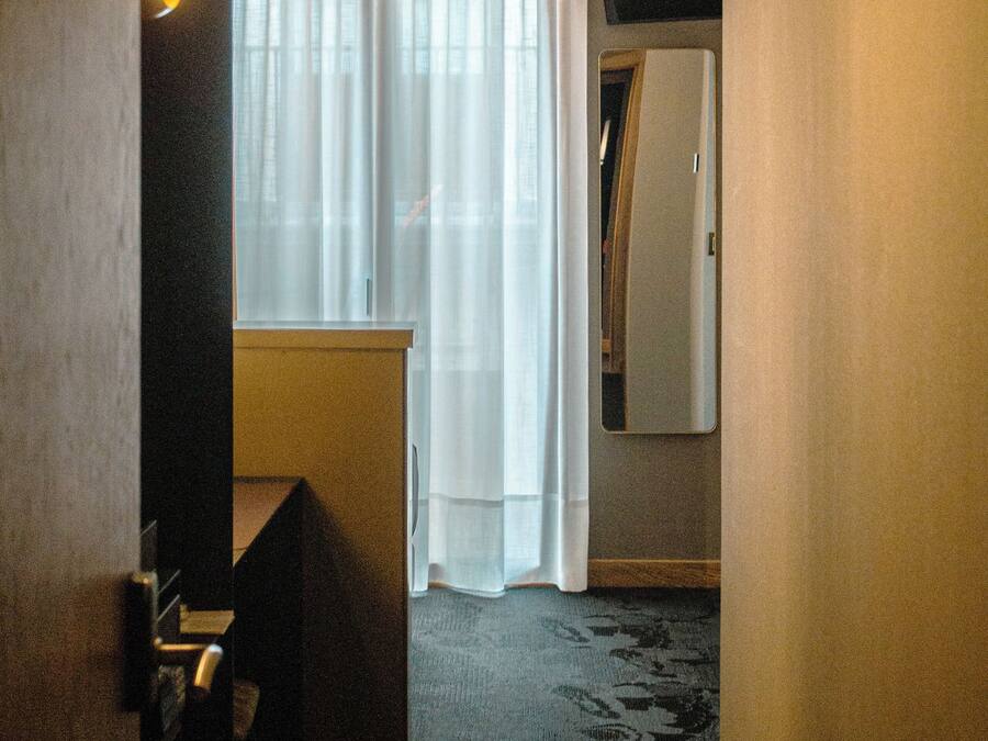 A hotel room with a bed, a desk, a chair, a mirror, and a window with curtains.