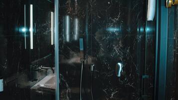Un baño moderno con cabina de ducha de vidrio, paredes de mármol y zona de lavamanos a la vista.