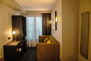 Una camera d'albergo con scrivania, sedia, divano e un'ampia finestra con tende.