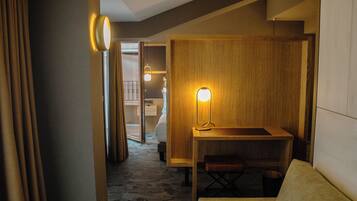 A hotel room with a wooden desk, a bench, a lamp, and a bed.
