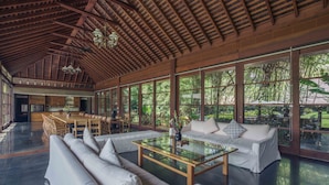 Una habitación amplia con techo alto, ventanas grandes, un comedor y una zona de estar con una mesa de centro de vidrio.