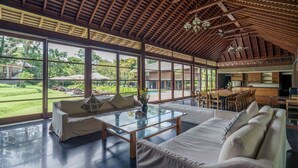 Amplia sala de estar con una mesa de centro de vidrio, sofás y vistas a un exuberante jardín y piscina.