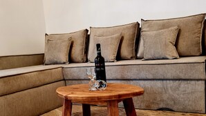 Ein runder Couchtisch aus Holz mit einer Flasche und einem Glas, vor einer beigefarbenen Couch mit Kissen platziert.
