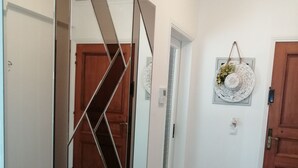 Ein Flur mit Holzboden, einer Bank und einem Spiegel, der den Raum widerspiegelt. Zwei Türen, an einer Wand befindet sich eine Dekoration.