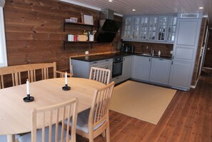 Een houten interieur met een eettafel, stoelen en een keuken met kasten en apparatuur.
