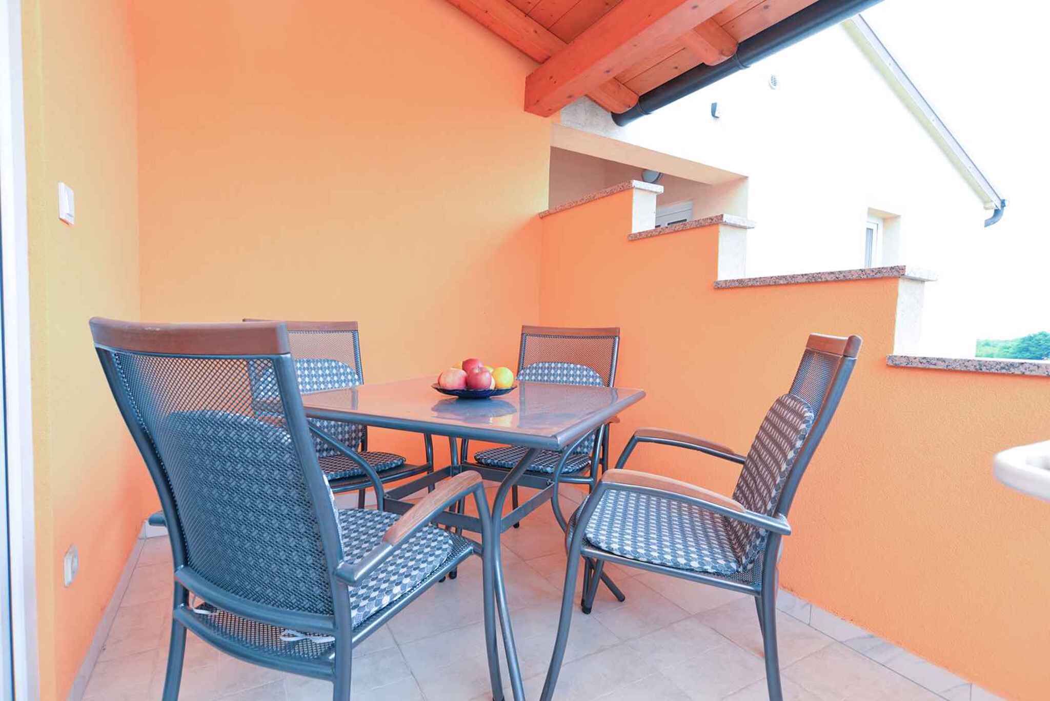 An outdoor patio with a table and chairs, a small fruit bowl, and a view of a building.