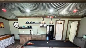 Un biliardo in una stanza con pavimento in legno, angolo cottura con mobili ed elettrodomestici, e un soffitto con decorazione in metallo ondulato.