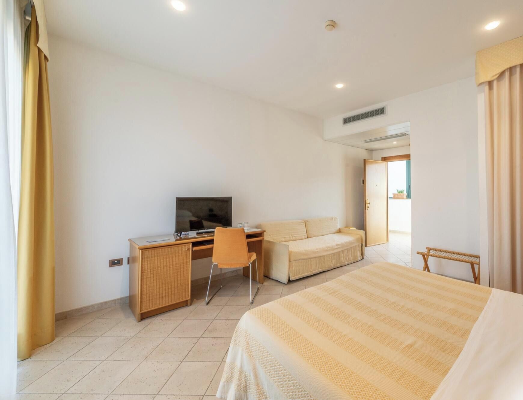 A hotel room with a bed, a desk with a television, a sofa, and a chair.